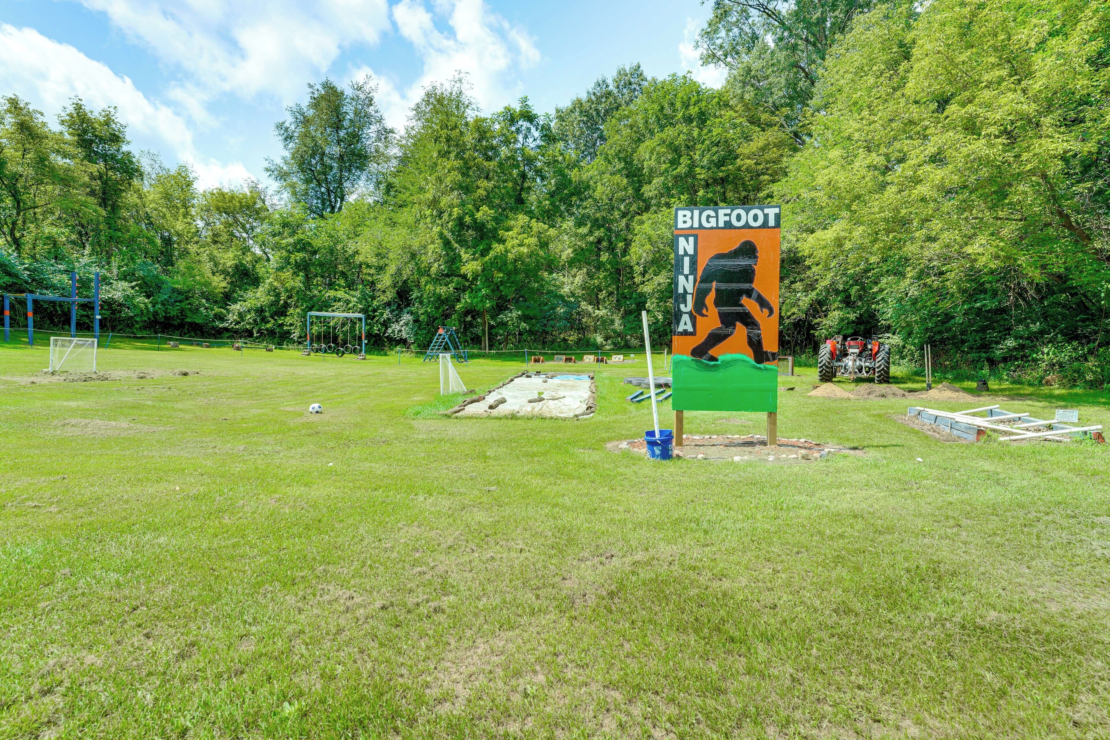 A grassy field with a playground, a soccer goal, and a sign with a person running.