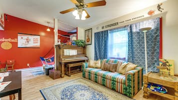 A living room with a red wall, a piano, a sofa, a patterned rug, and a ceiling fan.