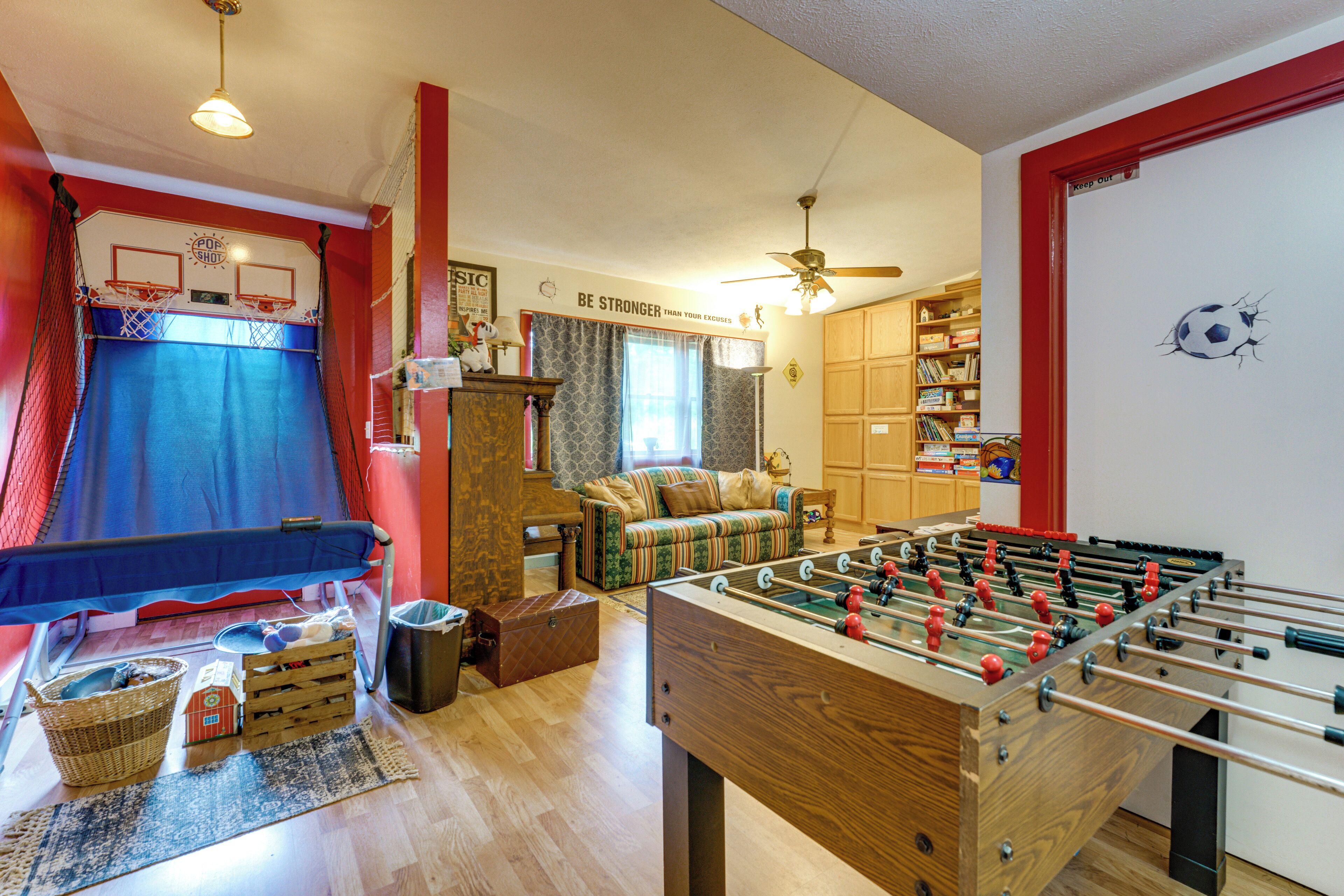A room with a foosball table, a basketball hoop, a sofa, and a bookshelf.