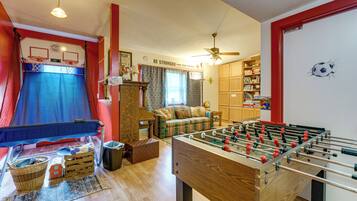 A room with a foosball table, a basketball hoop, a sofa, and a bookshelf.