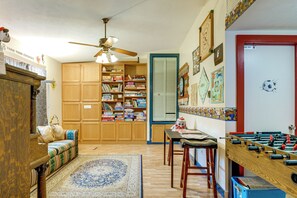 A room with a wooden cabinet, a ceiling fan, a bookshelf, a futsal table, and a patterned rug. - Southeast Michigan Escape w/ Outdoor Fun (Adrian)