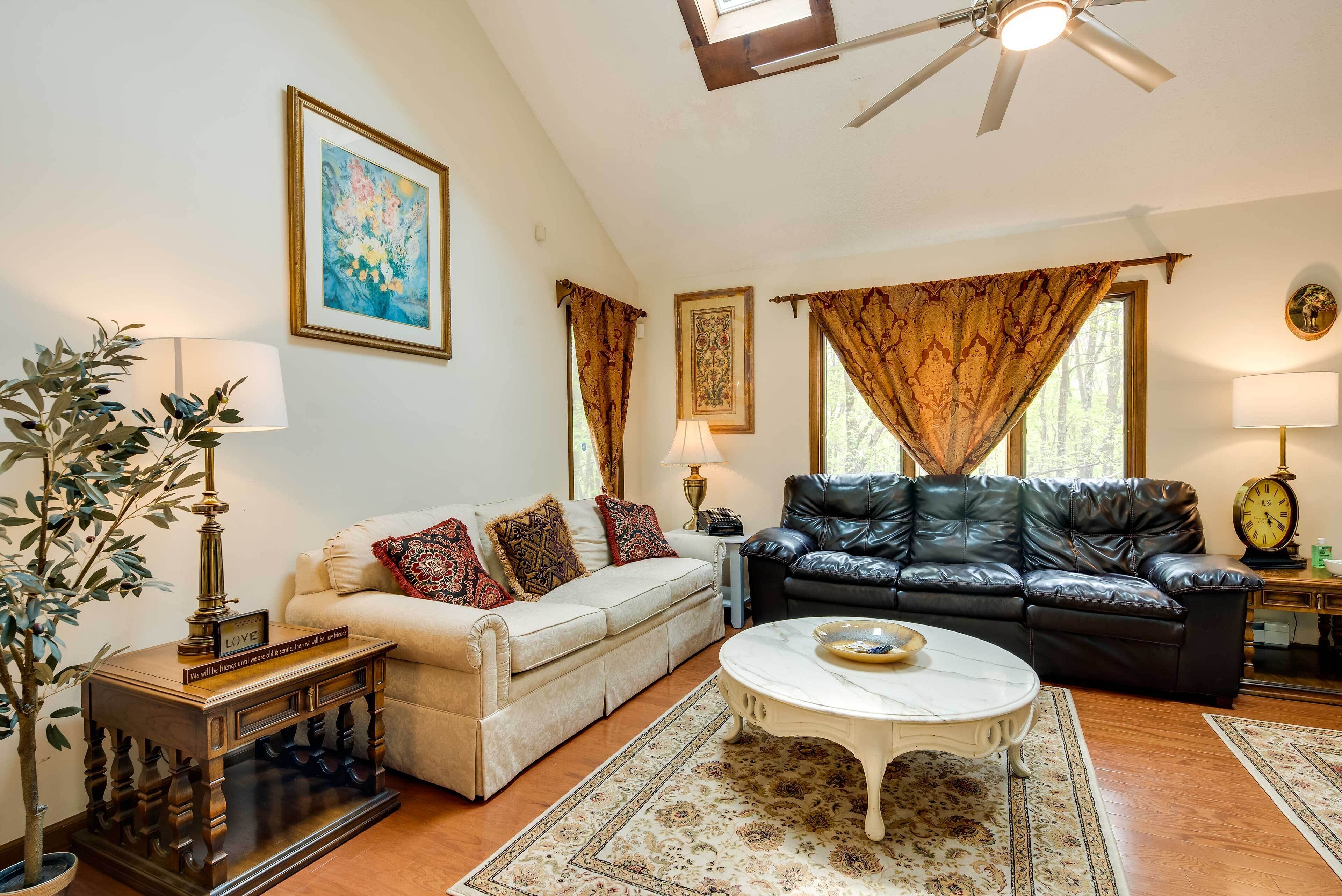 A living room with a beige sofa, a black leather couch, a white coffee table, and a large window with curtains.