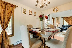Un'area pranzo con un tavolo in legno apparecchiato per quattro persone, circondato da sedie imbottite. Sul tavolo c'è un vaso con fiori, e un orologio appeso al muro.