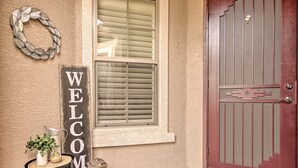 A welcome sign, a potted plant, and a lantern on a small table outside a door. - Goodyear Home w/ Pool: Near Golf & Ballpark! (Goodyear)