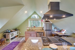 A kitchen with a gas stove, stainless steel appliances, and a window above the sink.