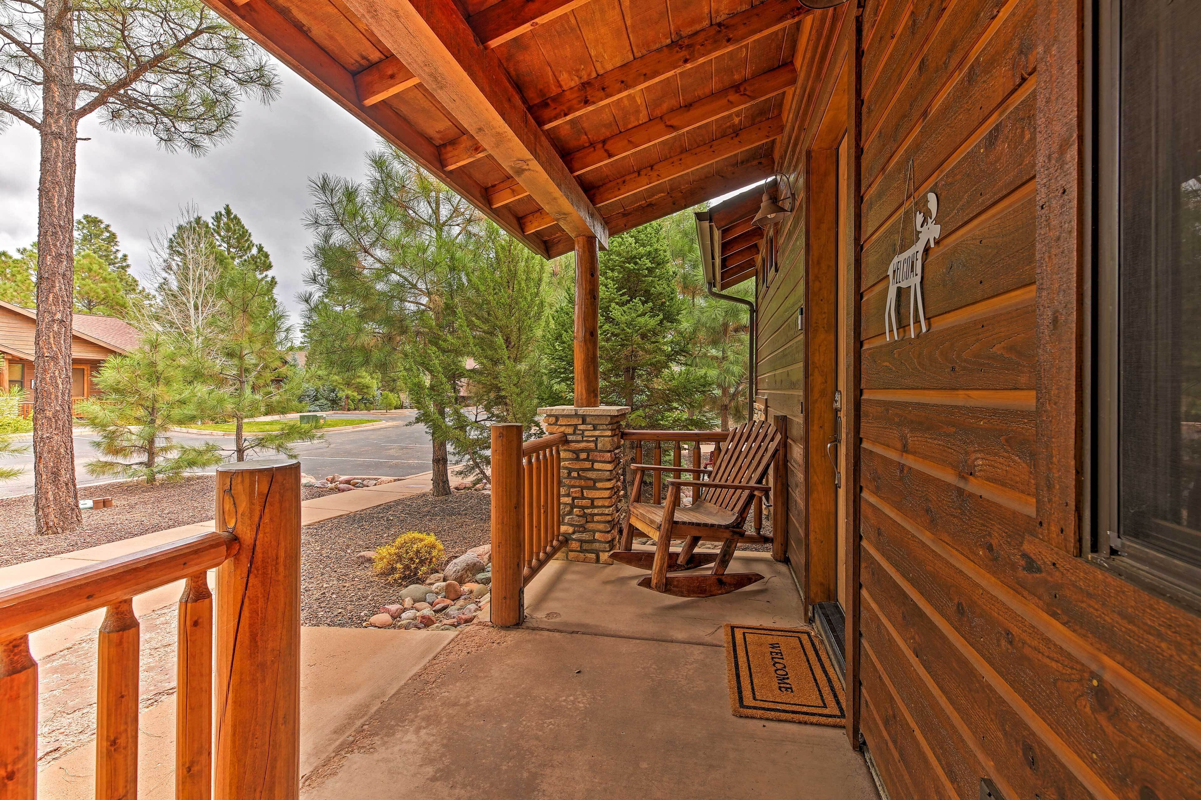 A wooden cabin with a porch, stone pillar, and two wooden chairs.