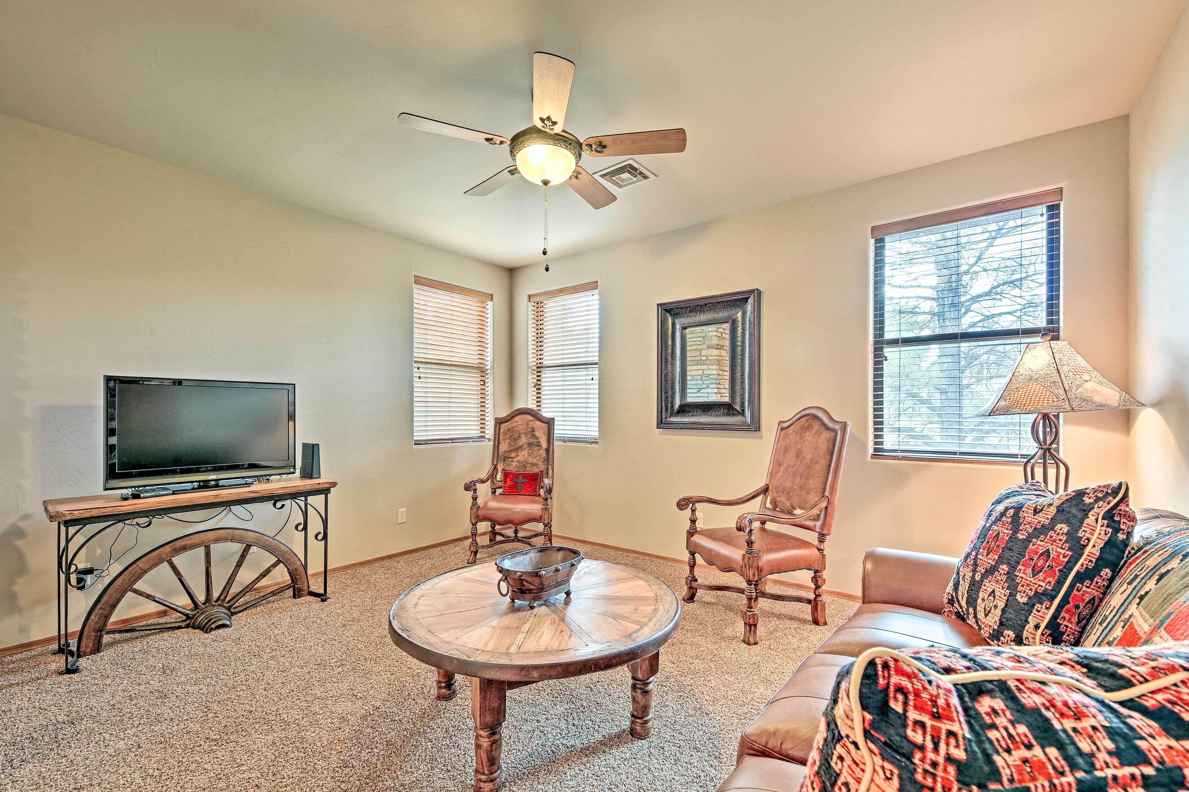 A living room with a TV, two chairs, a sofa, a table, and a ceiling fan.