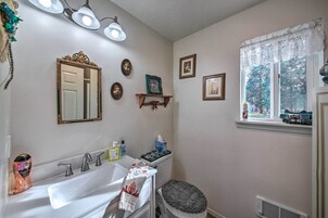 Un baño con lavamanos blanco, tocador con espejo y ventana con vista a árboles.