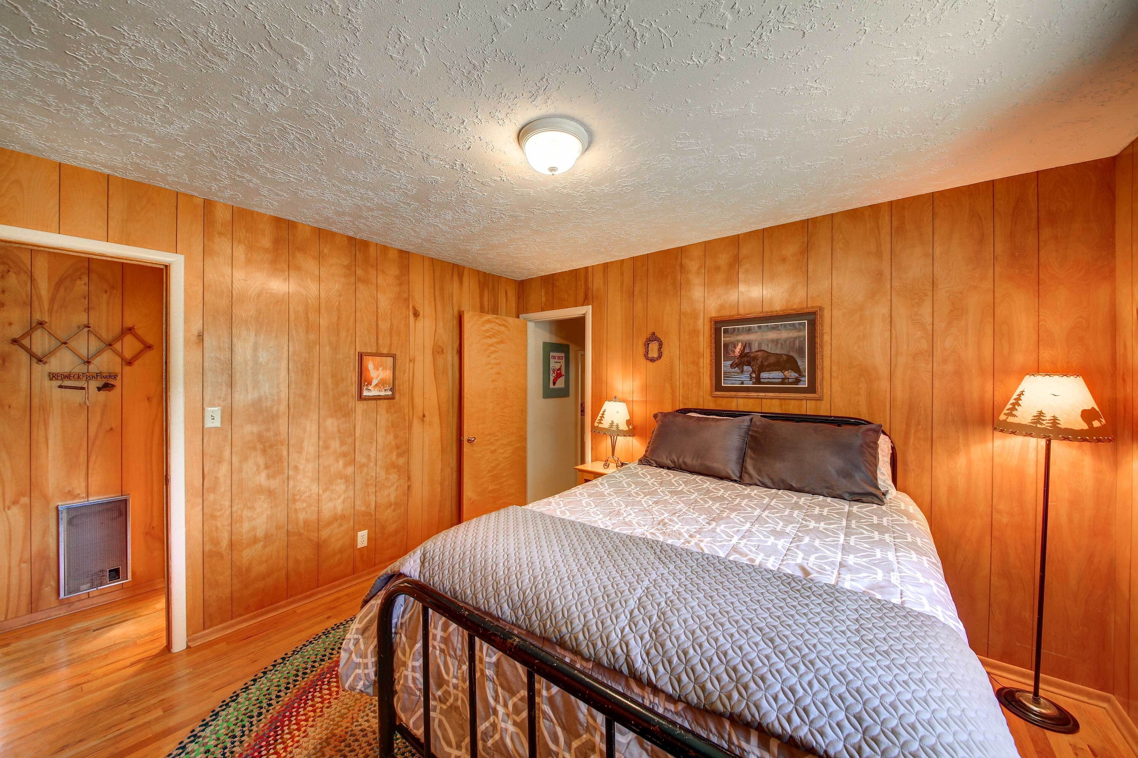 A bedroom with wooden panel walls, a bed with a patterned bedspread, two bedside lamps, and a framed picture on the wall.