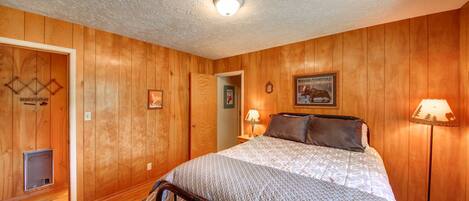 A bedroom with wooden panel walls, a bed with a patterned bedspread, two bedside lamps, and a framed picture on the wall.