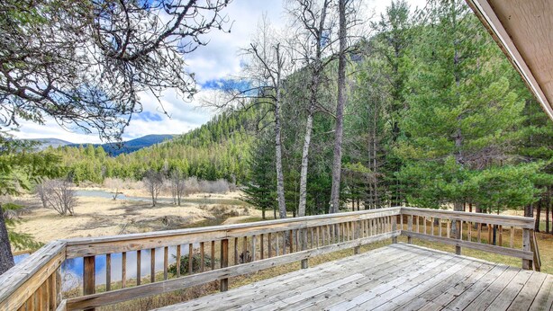 A wooden deck with a view of a forested area and a body of water. - Angler's Dream Remote Escape on Bull River! (Noxon)