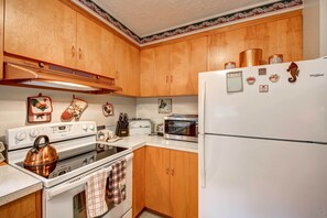 Una cocina con armarios de madera, un refrigerador blanco, una estufa, un microondas y diversos utensilios de cocina.