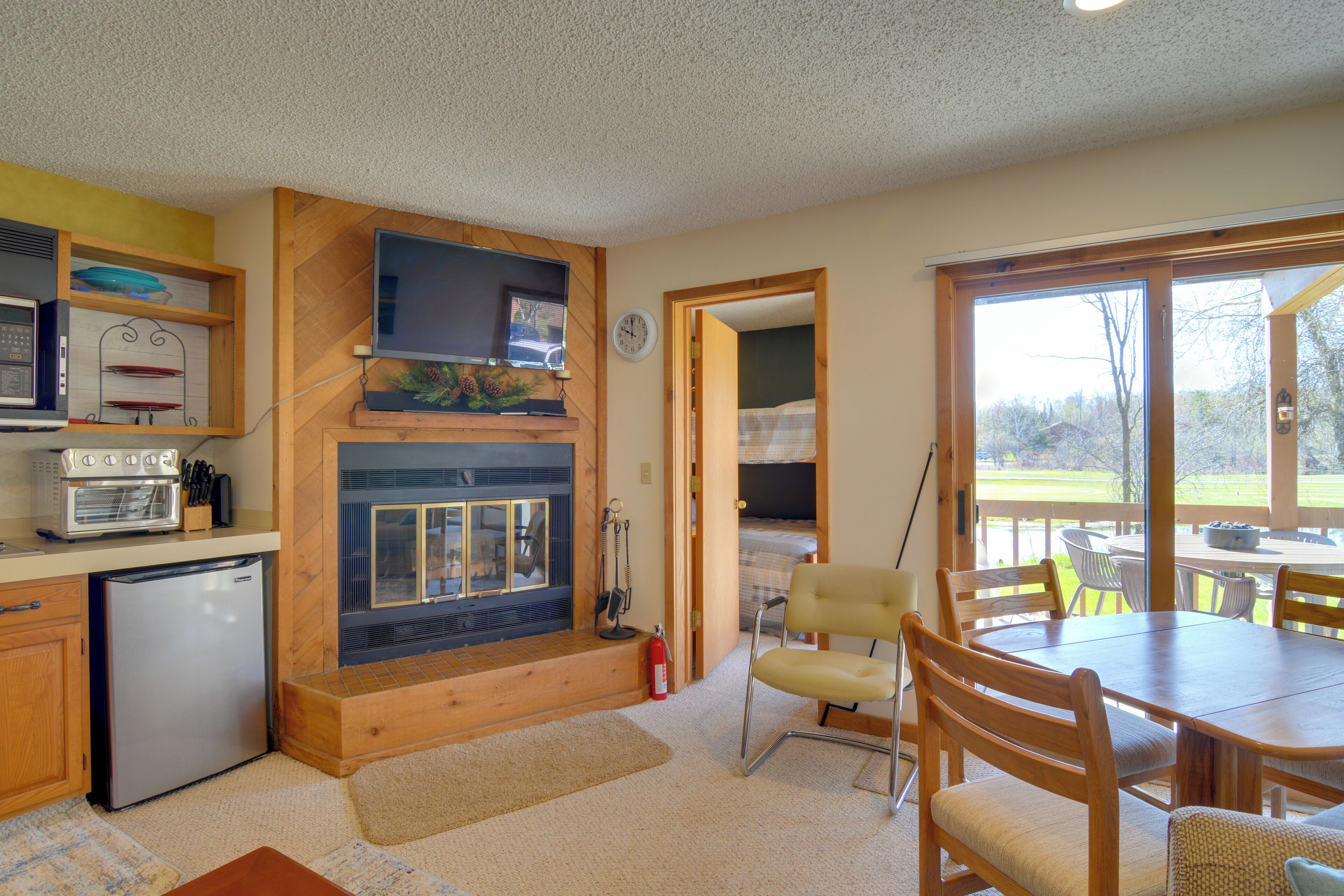 A kitchen with a built-in oven, a refrigerator, and a television above the oven. There is a dining area with a table and chairs.