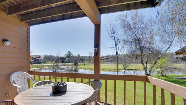 Eine Holzdar Terrasse mit Tisch und Stühlen, mit Blick auf ein Gewässer und eine begrünte Fläche mit Bäumen.