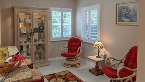 A cozy living room with a glass cabinet, two red chairs, a table with a basket, and a floral rug. - Pet-friendly Flagler Beach Home w/ Yard Near Beach (Flagler Beach)