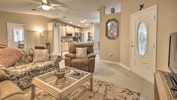 A living room with a sofa, armchair, and coffee table, a kitchen in the background, and a decorative door with a stained glass window. - Pet-friendly Flagler Beach Home w/ Yard Near Beach (Flagler Beach)