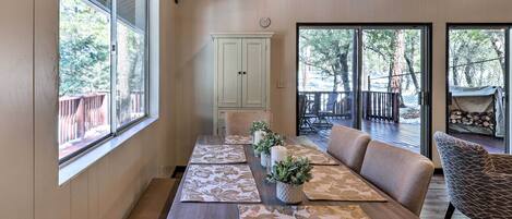 A dining area with a wooden table, cushioned seating, and large windows offering views of the outdoors.