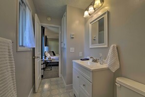 A bathroom with a white sink, a mirror, and a toilet. There is a towel hanging on the wall and a shower curtain partially open.