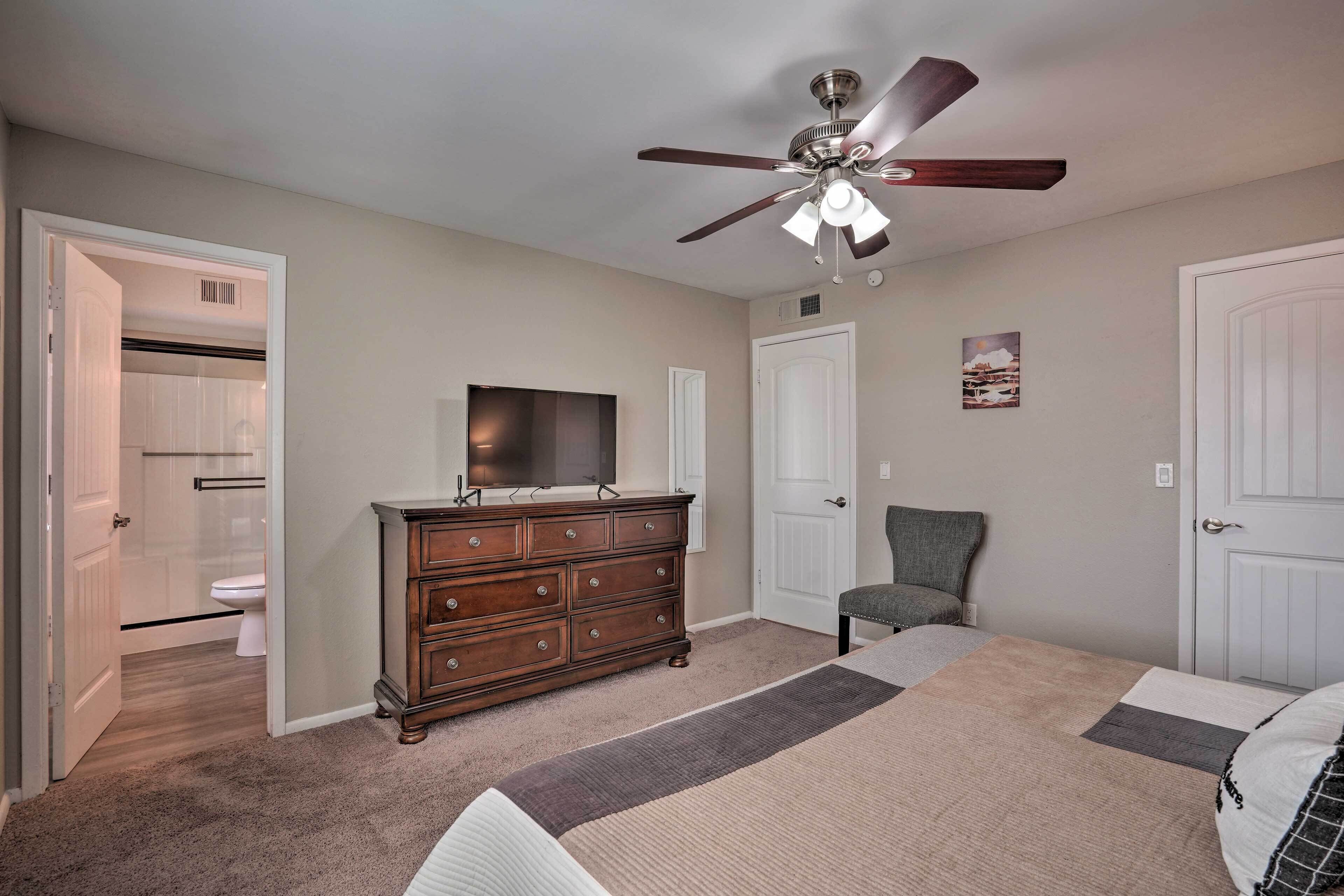 A bedroom with a bed, a dresser, a chair, a ceiling fan, and a television.