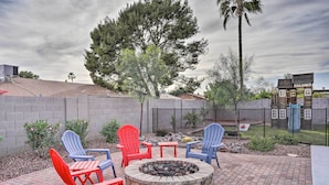 A patio area with a fire pit, red and blue Adirondack chairs, and a brick floor. - Phoenix Family Home w/ Pool + Playground! (Phoenix)