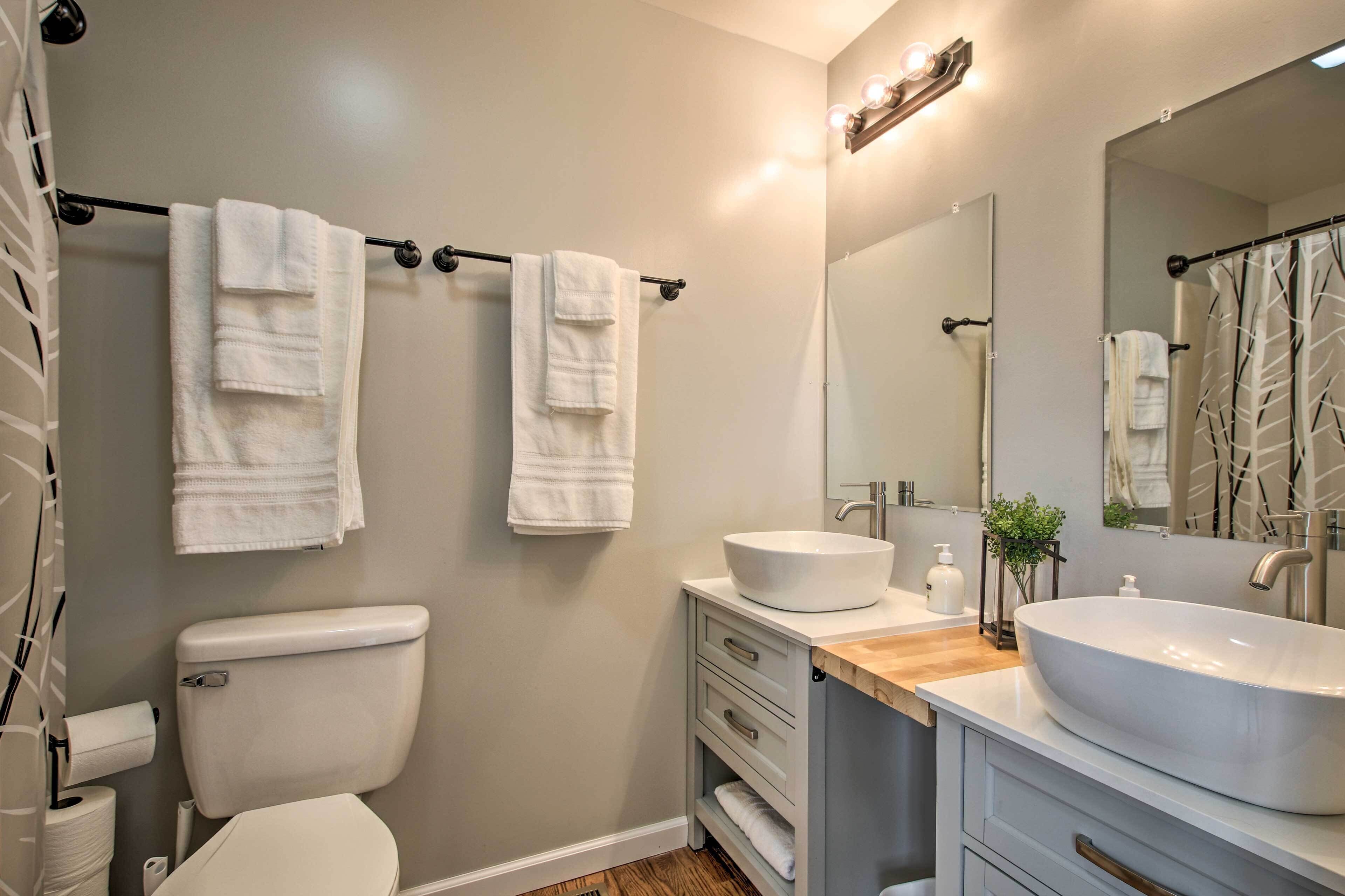 A bathroom with a toilet, two towels hanging on a rod, a sink with a mirror, and a shower curtain.