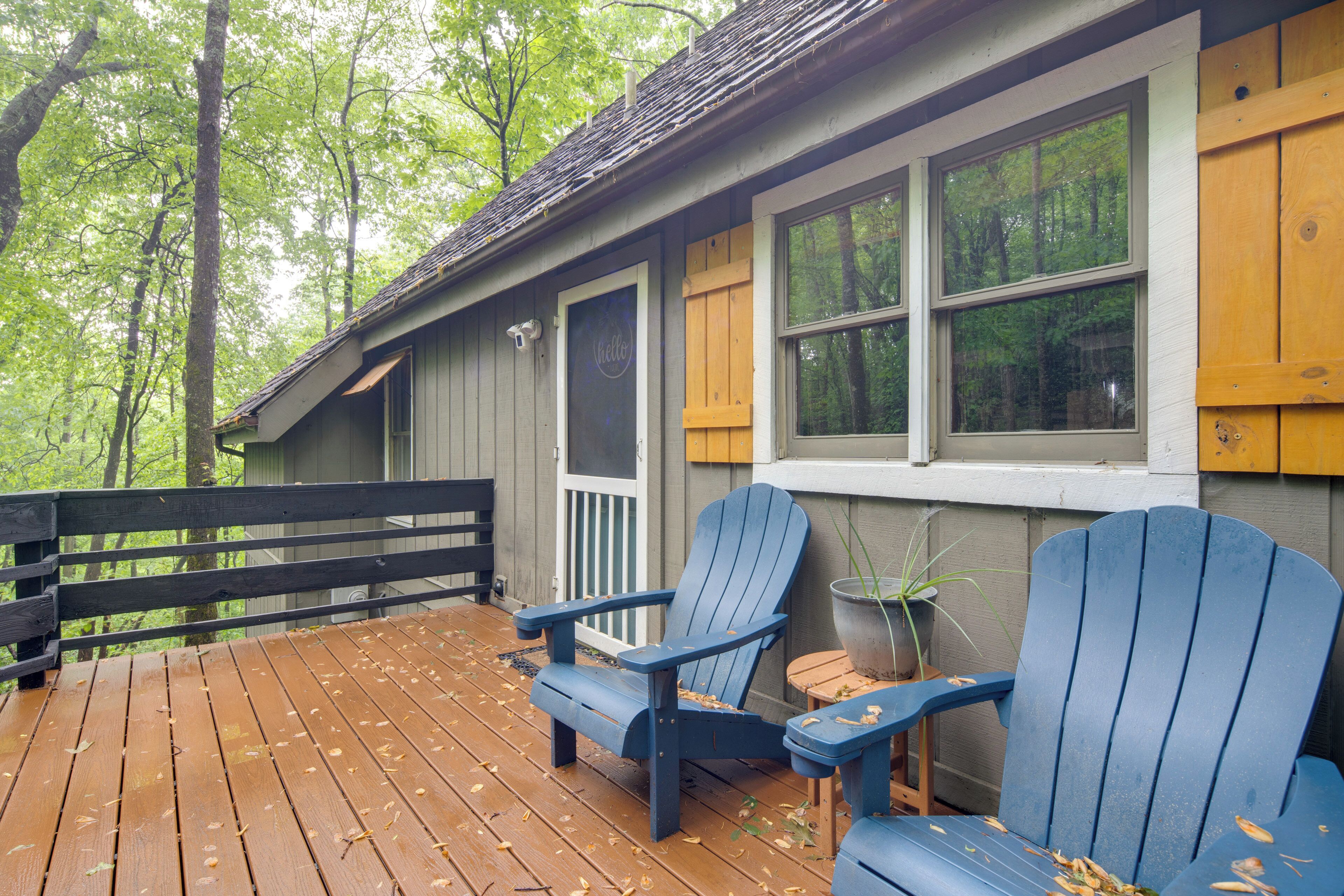 A wooden deck with two blue Adirondack chairs and a potted plant.