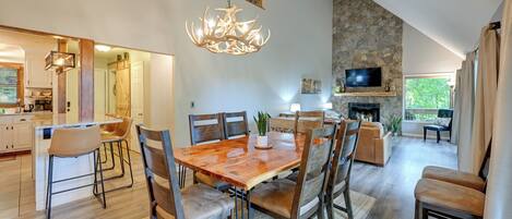 A spacious dining area with a wooden table and chairs, a chandelier, and a stone wall.