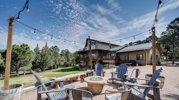 An outdoor seating area with Adirondack chairs and a fire pit, surrounded by a wooden deck and a building with a metal roof.