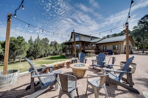 An outdoor seating area with Adirondack chairs and a fire pit, surrounded by a wooden deck and a building with a metal roof. - 'rocking Horse Ranch' 5BR Cabin in Payson (Payson)