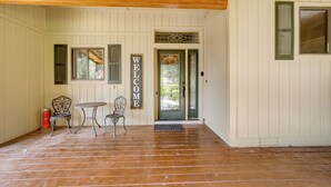 A wooden porch with a welcome sign, two chairs, a small table, and a fire extinguisher.