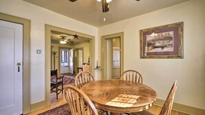 Un comedor con una mesa redonda de madera, seis sillas, un ventilador de techo y un cuadro en la pared.