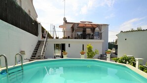 Une piscine à l’eau d’un bleu cristallin, entourée d’un mur blanc et bordée d’un bâtiment doté d’un balcon.