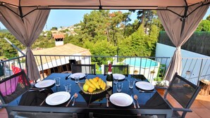 Une table mise pour quatre personnes, avec un panier de fruits, des assiettes, des couverts et une bouteille de champagne.