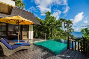 Relax on the balcony overlooking the ocean and pool, surrounded by lush greenery and palm trees.