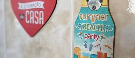 A wall with a heart-shaped sign reading "A COZINHA é a CORAÇÃO da CASA" and a vertical sign with a beach theme, including a drink and a straw.