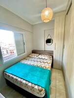 A bedroom with a bed, a window, a hanging light fixture, and a wardrobe.