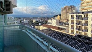 A balcony with a chain-link fence, tiled floor, and a view of surrounding buildings. - Apto Boqueirão próximo ao Mar (Praia Grande)