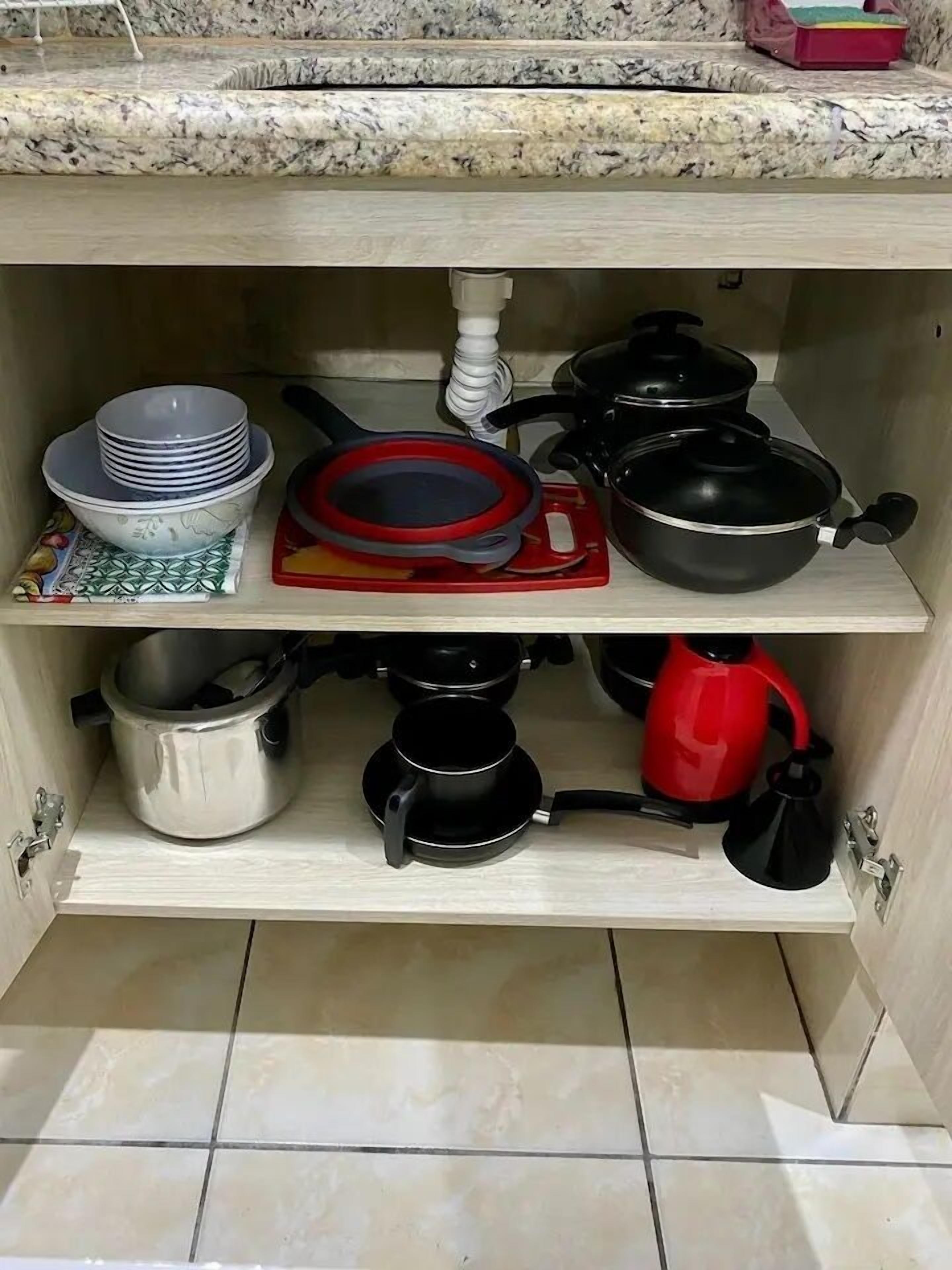 Uma cozinha com bancada de granito, pia e diversos utensílios de cozinha, incluindo panelas, frigideiras e chaleira.