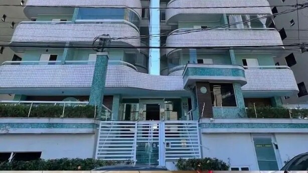 A multi-story residential building with balconies, a gated entrance, and a tiled ground floor. - Apto Boqueirão próximo ao Mar (Praia Grande)