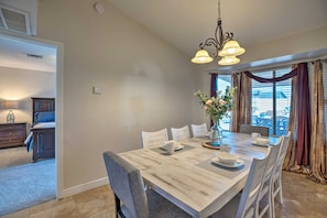 A dining area with a large wooden table, white chairs, and a chandelier.
