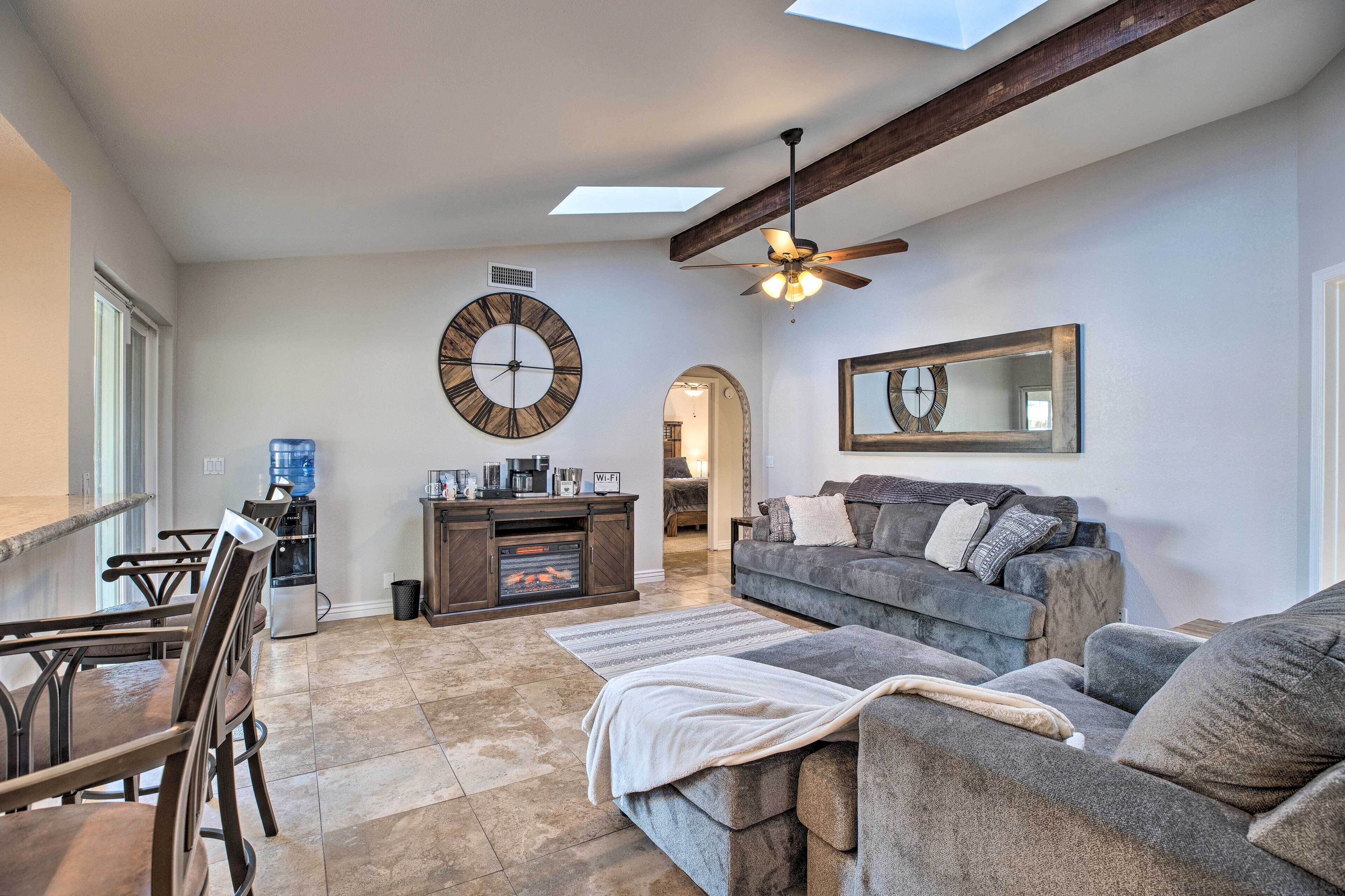 A spacious living area with a fireplace, a large clock, and a ceiling fan.