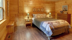 Ein Schlafzimmer einer Holzhütte mit einem Bett, zwei Nachttischen, einer Kommode und gerahmten Bildern an der Wand.