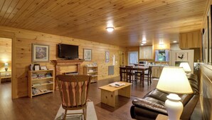 Ein Zimmer mit Holzvertäfelung, einem Fernseher, Bücherregalen, einem Ledersofa und einem Essbereich.