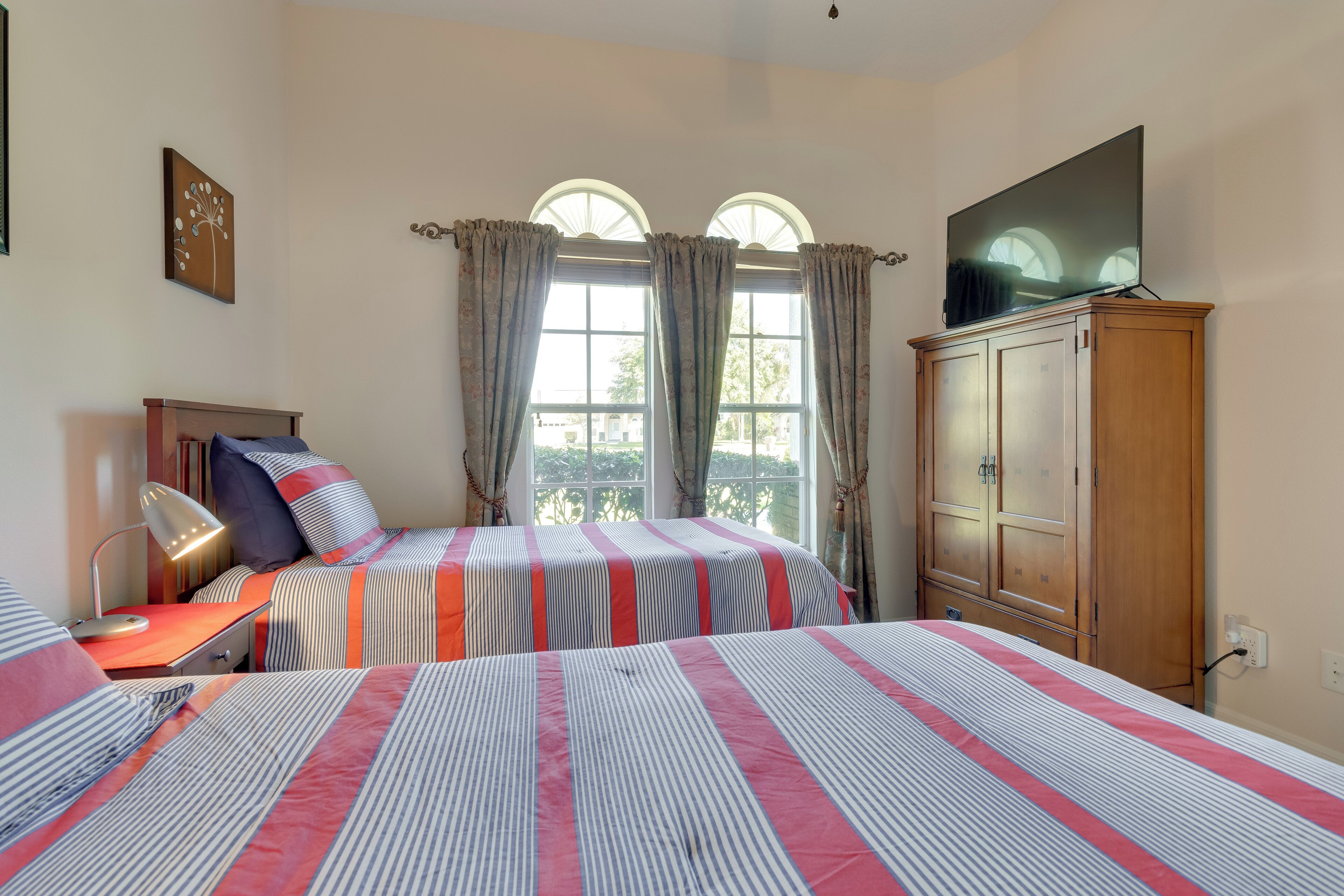 A bedroom with two beds, a wooden wardrobe, a desk with a lamp, and a TV on a stand.