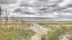 En sti af sand der fører til havet under en overskyet himmel.
