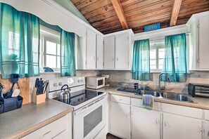 Cuina amb armaris blancs, una cuina, un forn microones i un rentaplat. Hi ha cortines color turquesa, un cartell blau amb números i una finestra.