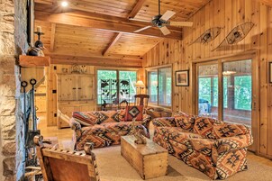 Un interior de cabaña acogedor, con techo de madera, un conjunto de sofás, una chimenea y ventanas grandes.