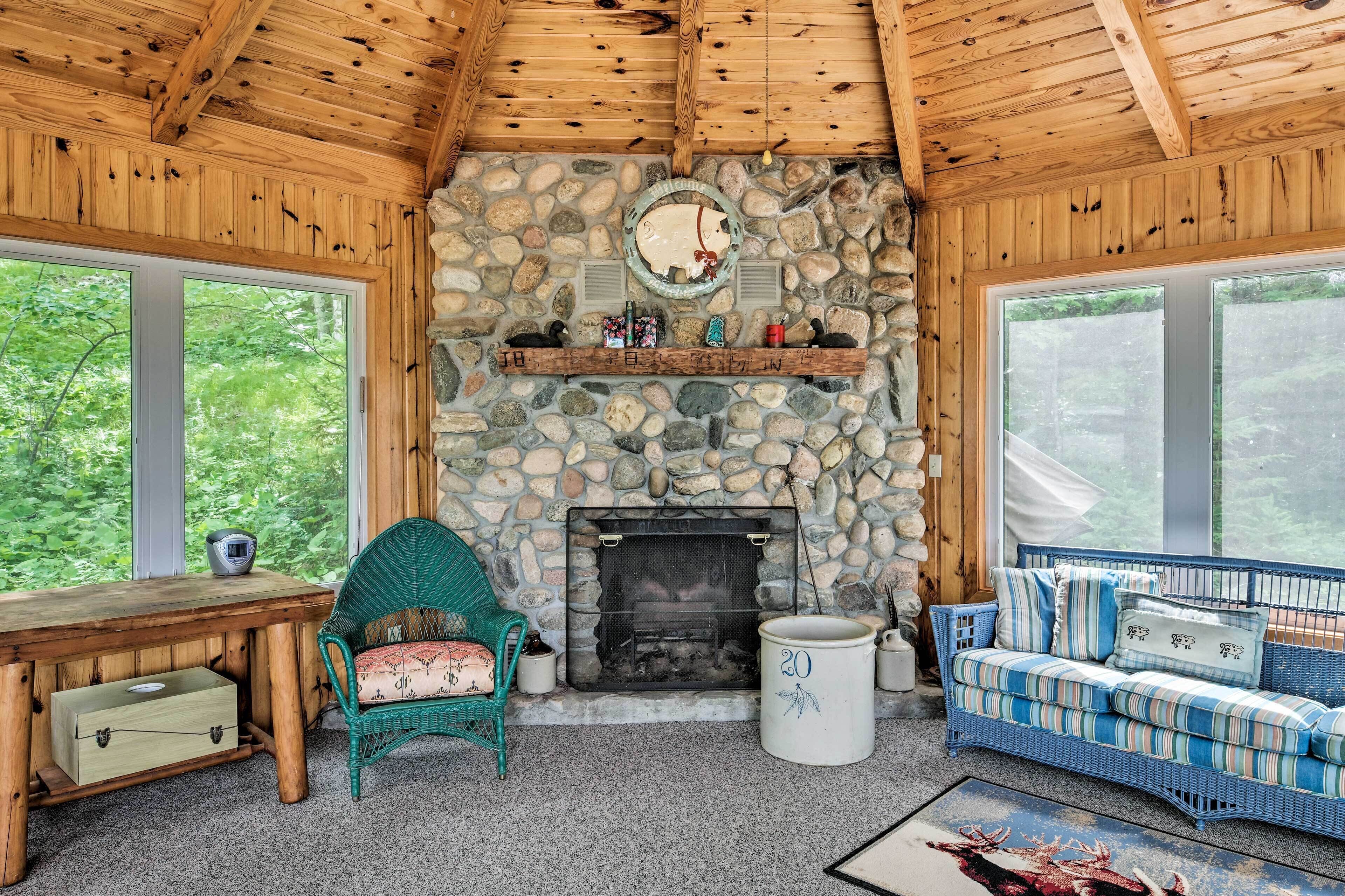 Una habitación acogedora con chimenea de piedra, techo de madera y grandes ventanales con vistas al follaje.