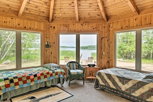 Una cabaña con dos camas, un escritorio y grandes ventanales con vistas a un lago.