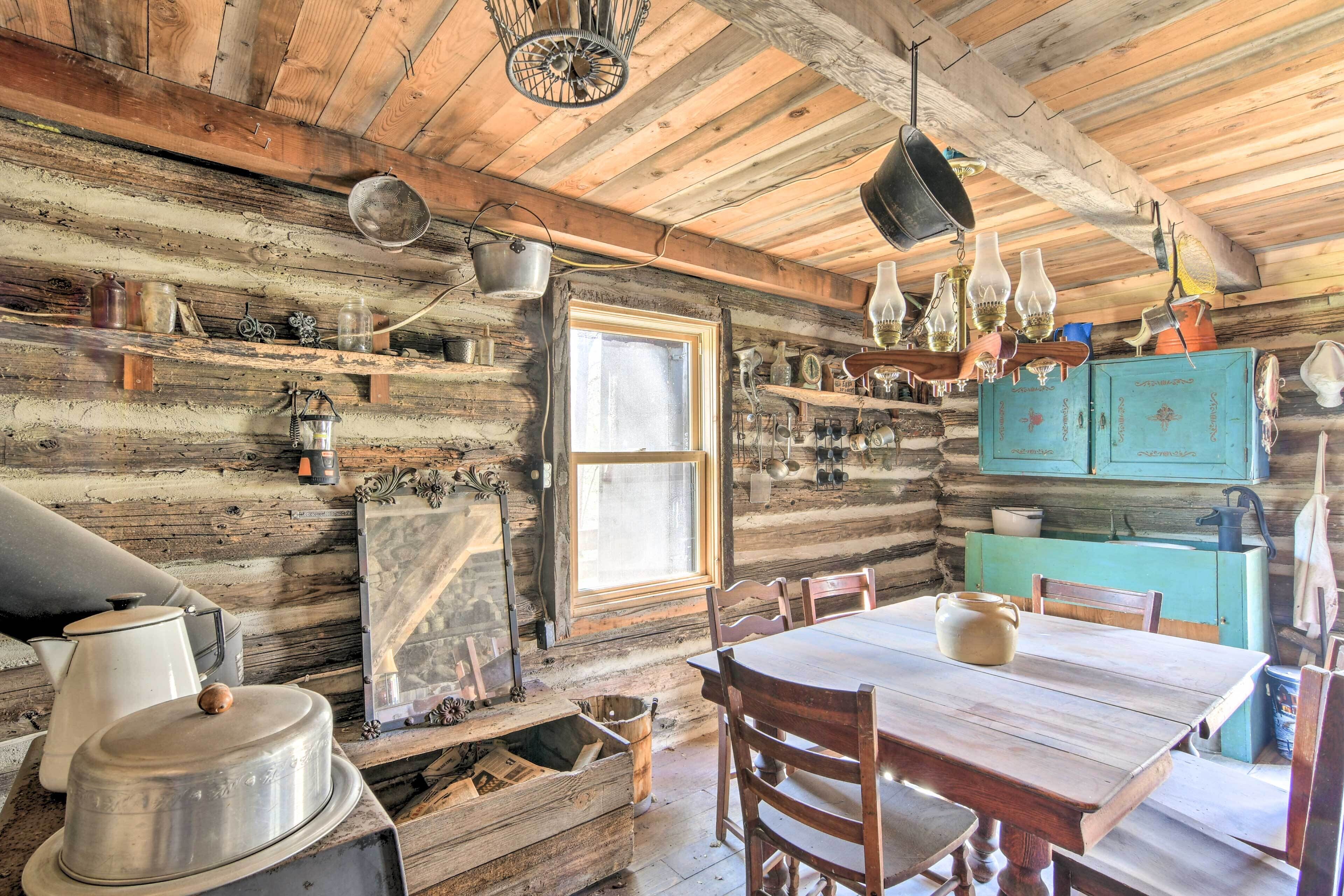 A rustic cabin interior with wooden walls, a wooden dining table, and various kitchen utensils and decorations.